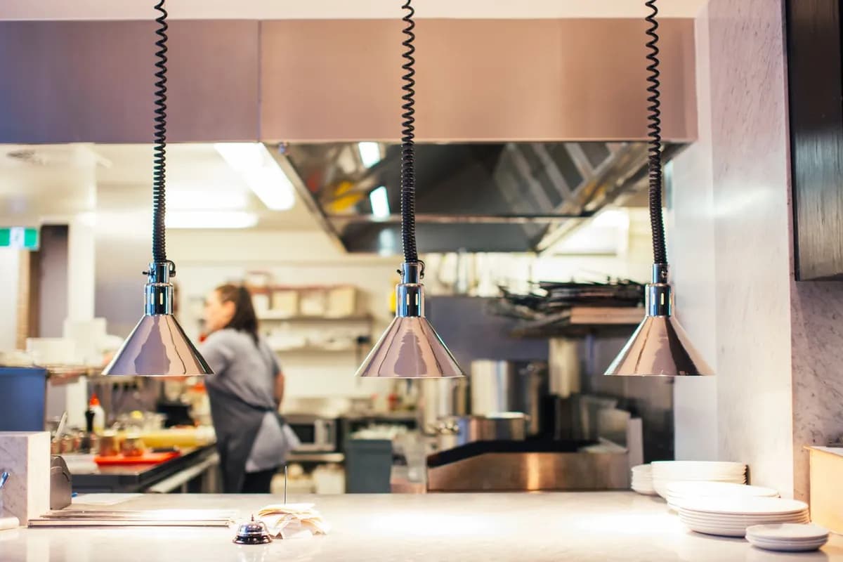 Restaurant kitchen pass with heat lamps and a cook at work